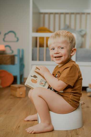 Enfant qui rit, assis sur son pot avec un livre
